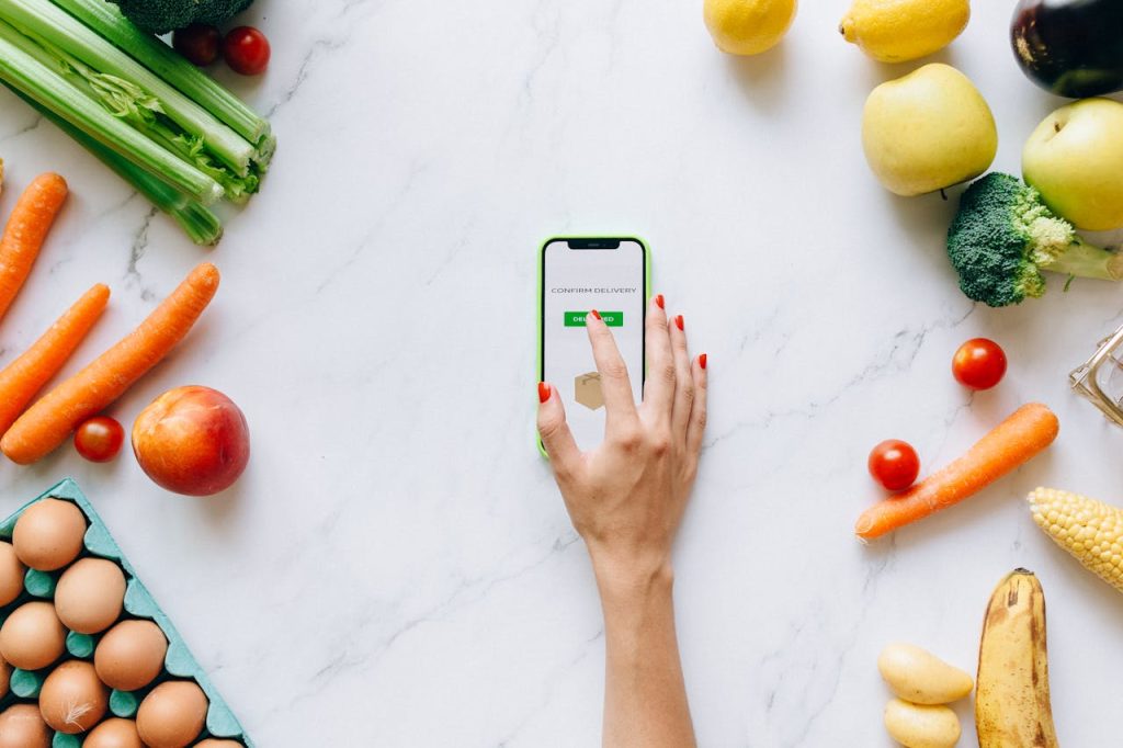 Flat lay of fresh vegetables and fruit with a smartphone showing grocery delivery confirmation.